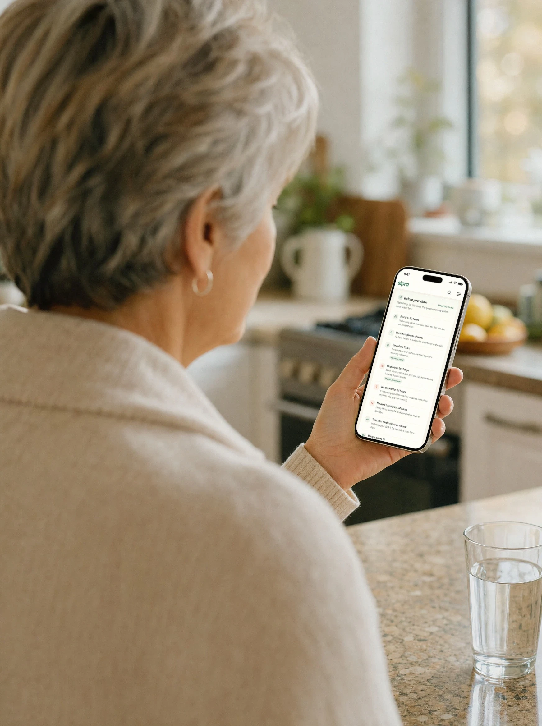 Over the shoulder, a member in her kitchen holding her phone open on Before your draw